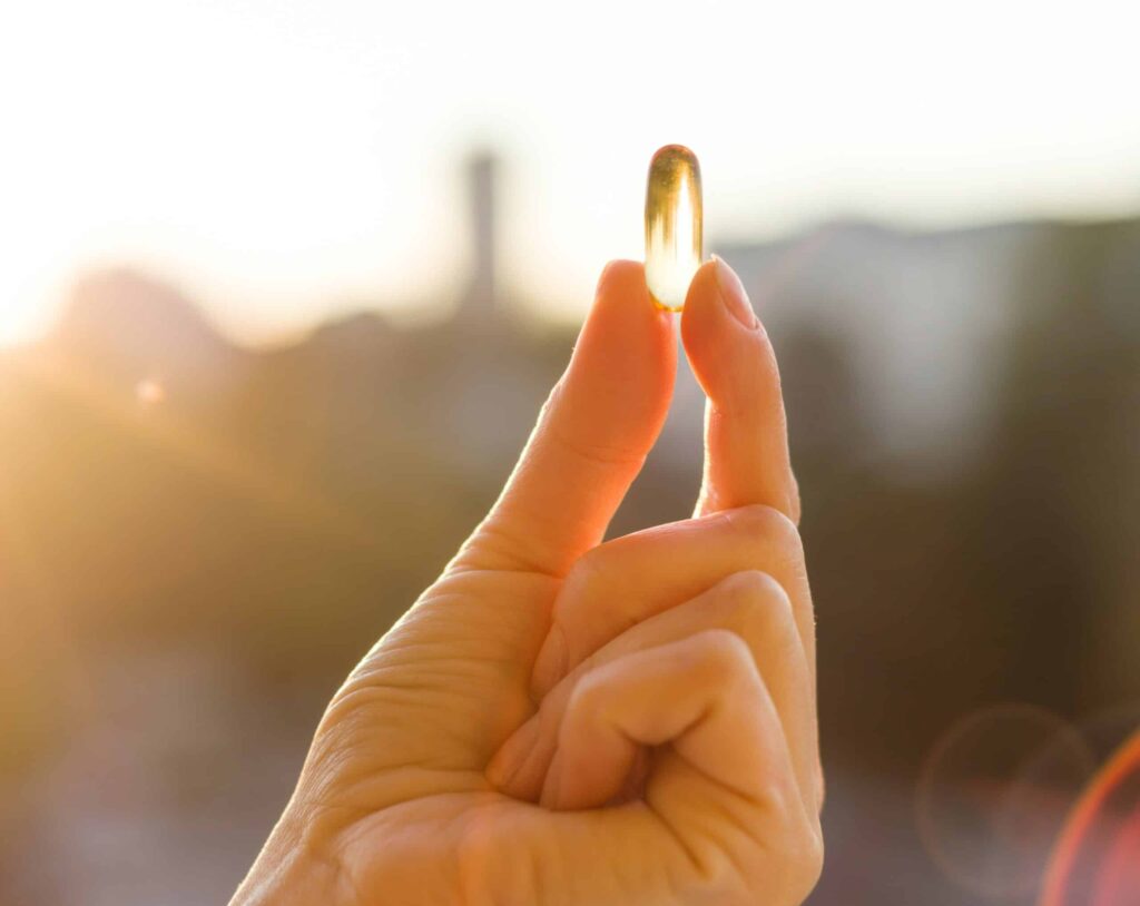 Mano adulta sujetando un capsula blande de omega 3 con un fondo urbano desenfocado