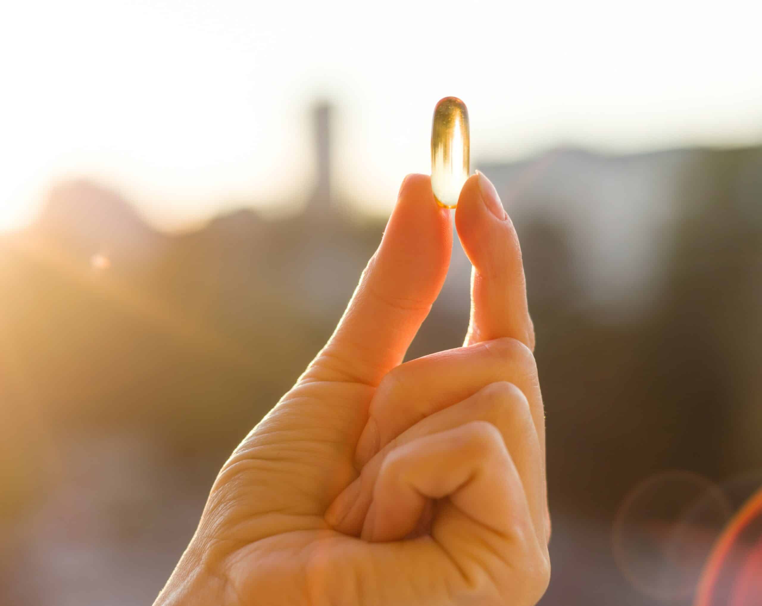 Mano adulta sujetando un capsula blande de omega 3 con un fondo urbano desenfocado
